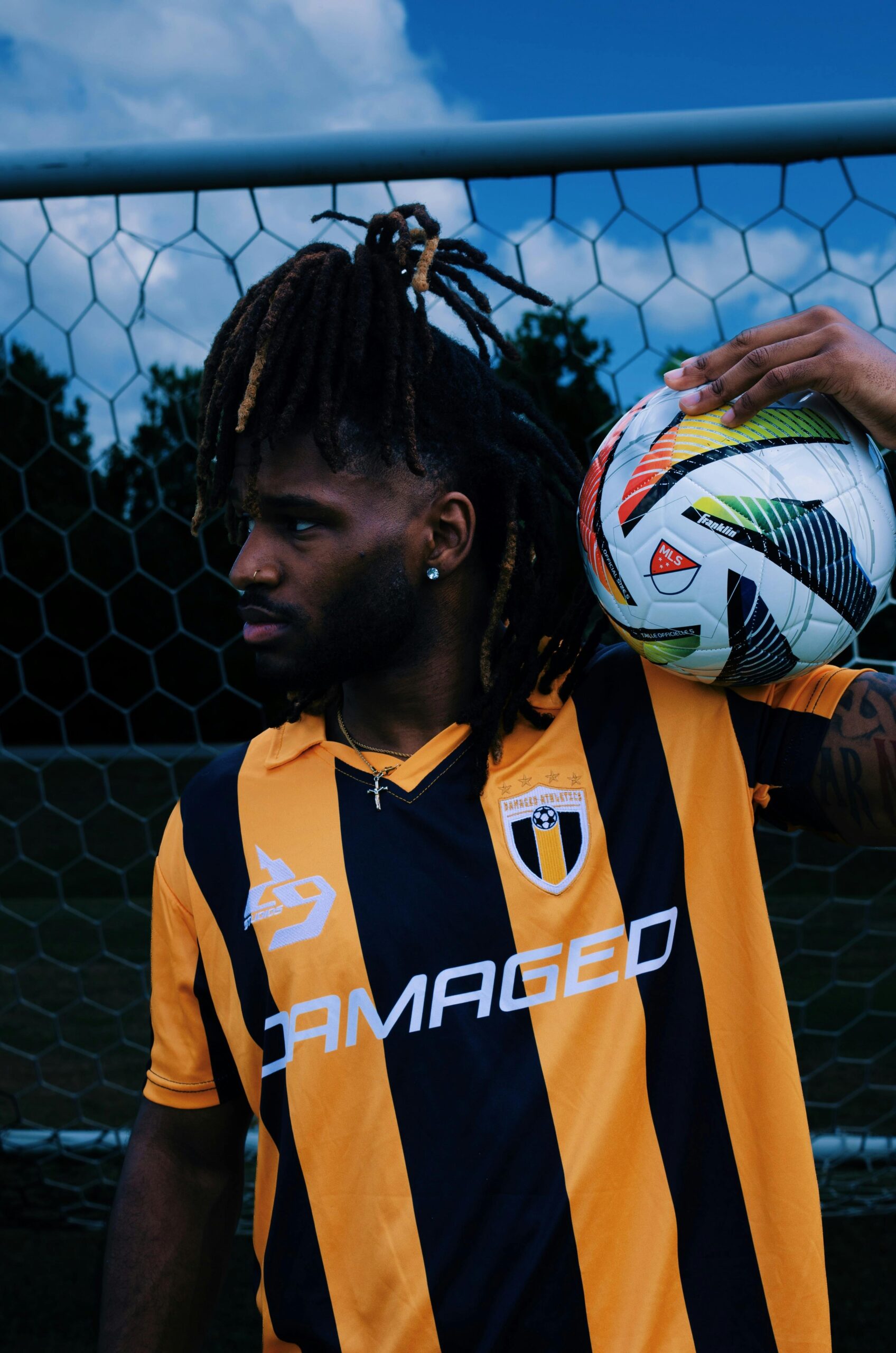 Male soccer player in black and yellow jersey holding a ball at the goalpost.