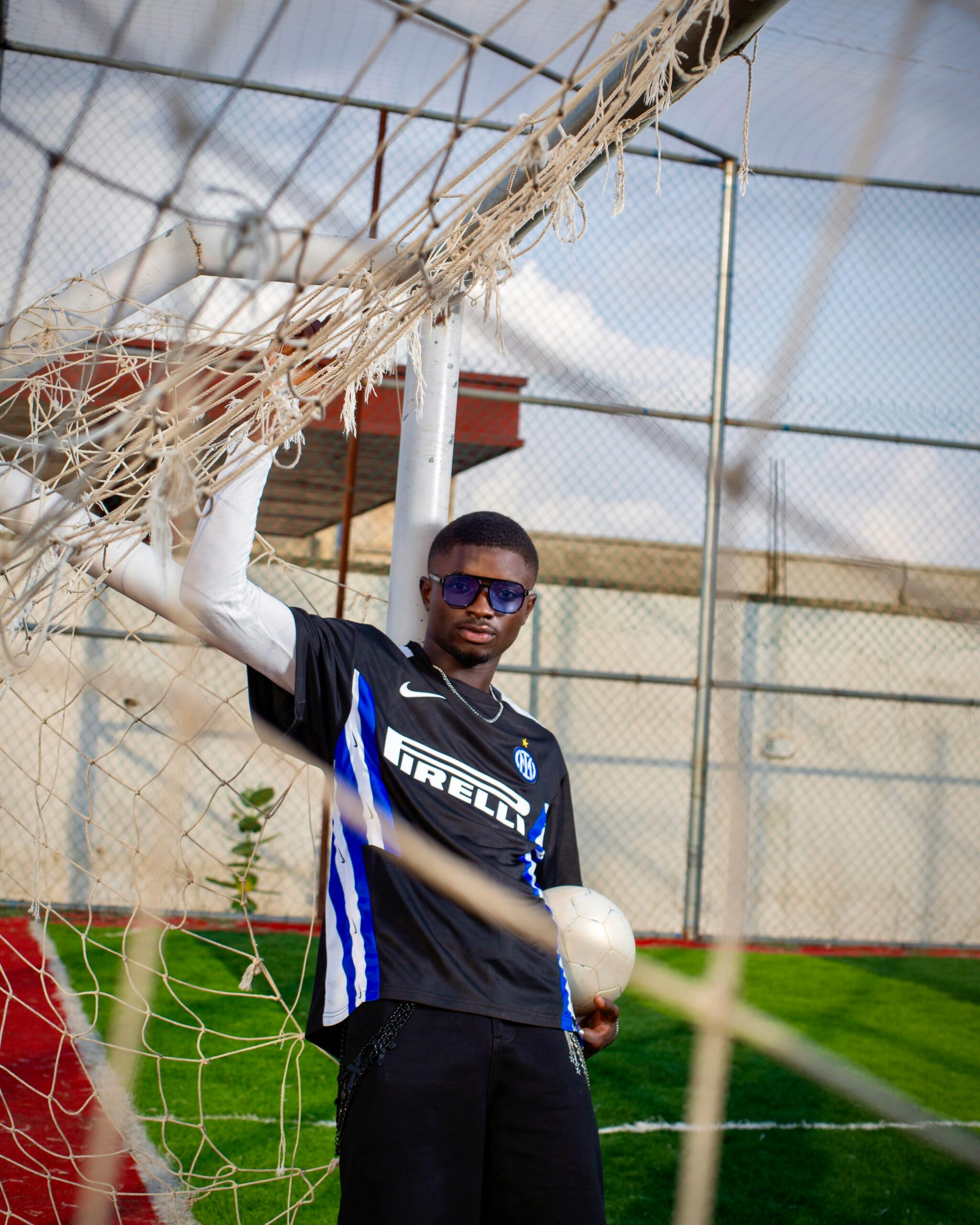 A young male footballer in sports attire posing confidently next to a goal on a sunny day.